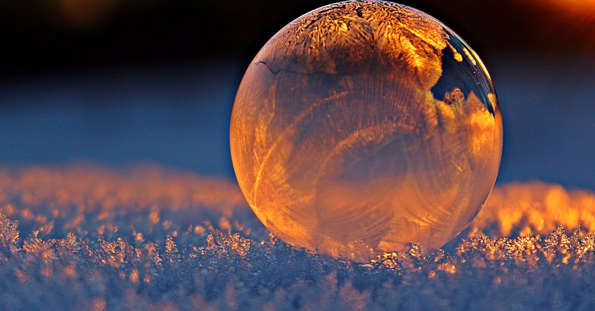 Close-up shot of a frozen bubble with warm reflections resting on a snowy surface at twilight.
